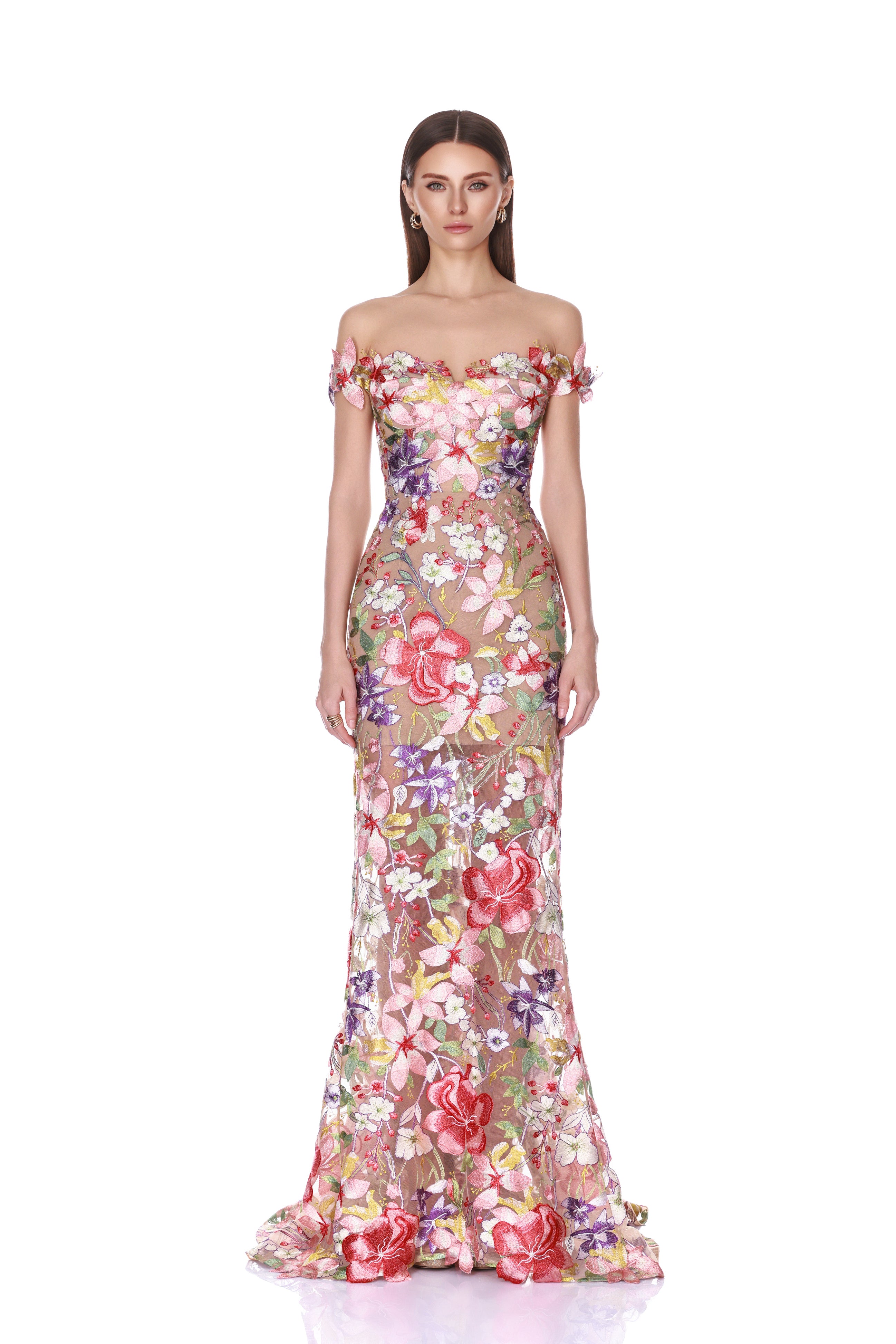 A model wearing a floor-length off-the-shoulder gown with a dense 3D floral applique pattern in pink, red, green, and purple on a sheer nude mesh base, set against a plain white background.